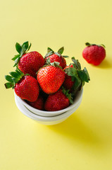 Heap of fresh ripe strawberries in a white bowl on a yellow background. Top view and copy space. Organic food concept.