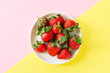 Fresh ripe strawberries in a white plate on a duotone background. Top view and copy space. Organic food concept.