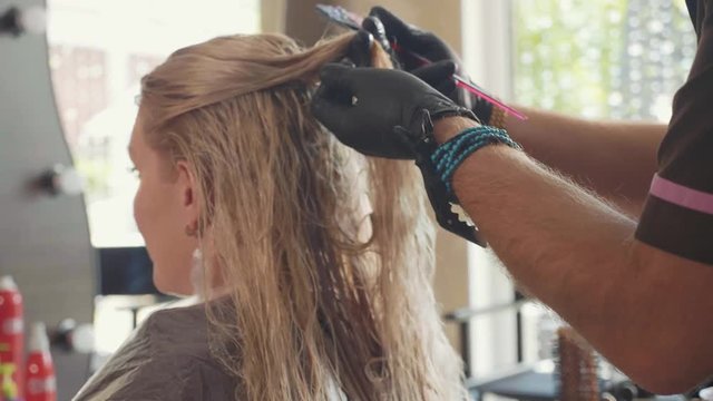 Hairdresser is untangles the hair of blond female customer at beauty spa salon