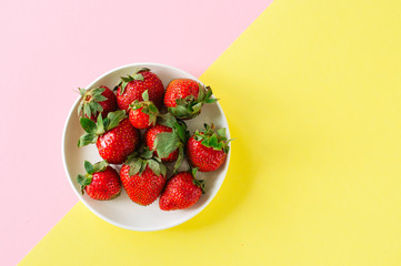 Fresh ripe strawberries in a white plate on a duotone background. Top view and copy space. Organic food concept.