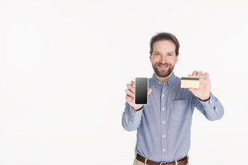 portrait of smiling bearded man showing smartphone with blank screen and credit card in hands isolated on white