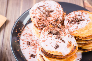 A pile of pancakes stuffed with fruit yoghurt and sprinkled with grated chocolate on a plate on a wooden table