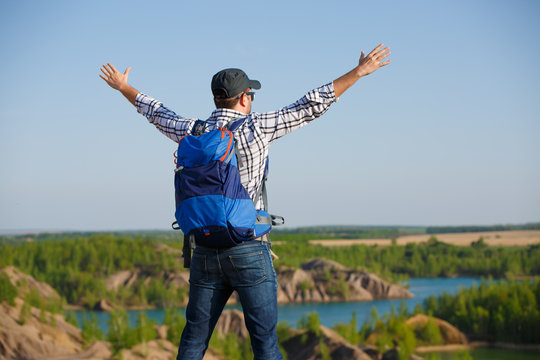 Image back of tourist man with backpack ,hands up on hill in background of mountain expanses, blue sky