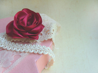Red rose from a satin ribbon handmade on a pink box, beige braid