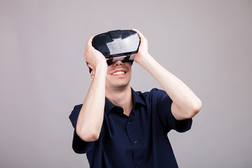 Excited man experiencing virtual reality for the firts time. He is wearing a VR headset. Gray background. Studio photo
