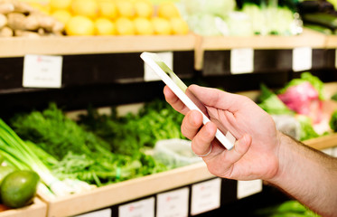 Cropped photo of male hands with phone in supermarket. Shop list