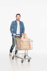 smiling man with shopping cart full of paper packages with grocery isolated on white