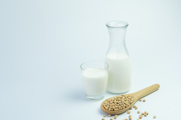 Homemade soy milk in glass bottle with soybeans in wooden spoon on white background
