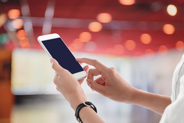 Woman hands holding and using smartphone with blank screen for your text or advertising isolated on blurred cinema theater interior background.Mock up phone mobile concept.