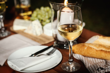 romantic dinner with a glass of wine, a baguette and snacks on an old wooden table on a summer evening