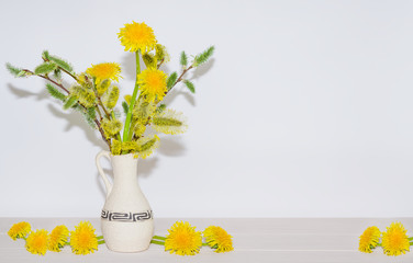 Bouquet of spring willow branches with dandelion flowers in a vase on a light background,...