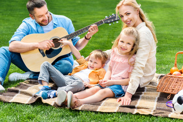 Fototapeta premium happy family playing guitar and sitting together on plaid at picnic