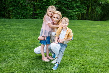 Fototapeta premium happy mother hugging adorable kids and smiling at camera in park