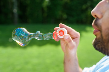 side view of bearded man blowing soap bubbles in park
