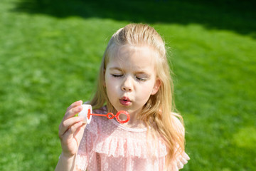 adorable little child blowing soap bubbles in park
