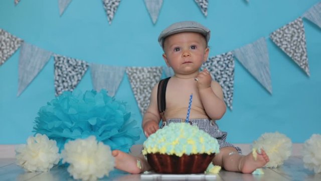 Little baby boy, celebrating his first birthday with smash cake party, studio isolated shot on blue background