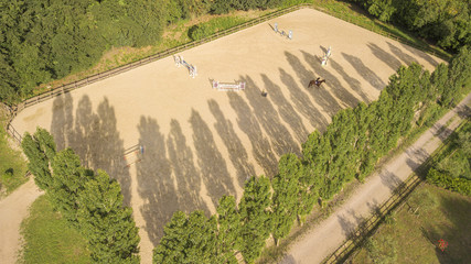 Aerial view of a riding field with fence and obstacles to train horses. In this sports facility,...