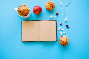 Chocolate chip muffins, notebook, earphones and chewing gums on a blue background, top view.