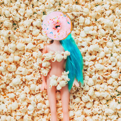 Blue haired plastic girl doll with a donut instead of a face on popcorn. Contemporary art collage.
