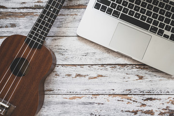 Laptop computer with ukulele guitar on wooden desk