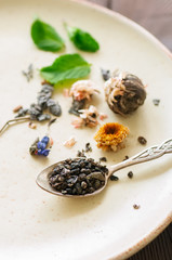 Assortment of dry green and flower tea in a plate. Wooden background.