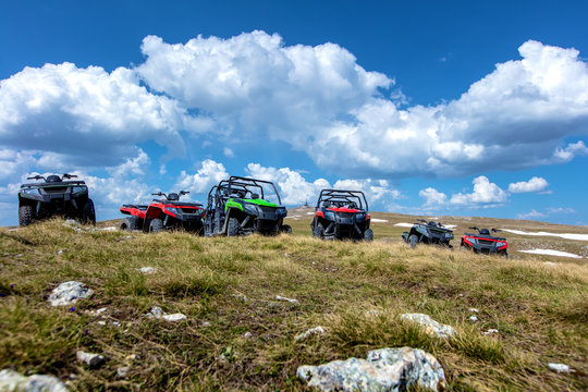 Parked ATV and UTV, buggies on mountain peak with clouds and blue sky in background