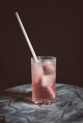 longdrink glass with white straw in rose coloured cocktail with black background