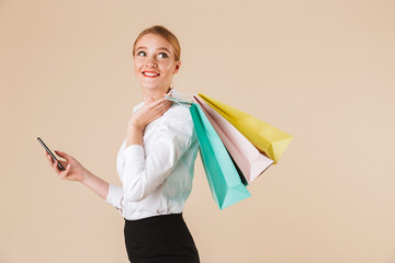 Cheerful young business woman holding shopping bags using mobile phone.