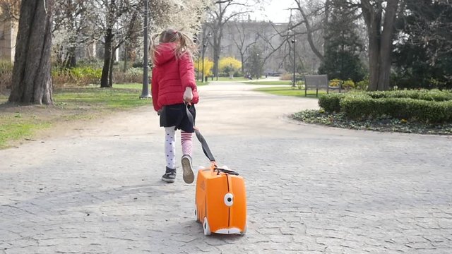 Smal kid girl have fun running in park with little travel suitcase slow motion