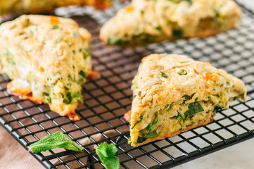 Savory scones with feta mozarella and green herbs on a wire rack. White stone background.