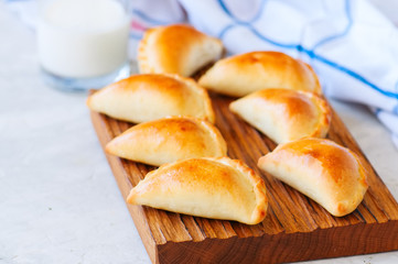 Homemade potato stuffed empanadas on a wooden board and glass of milk. White stone background.