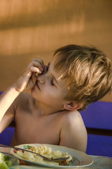 Blond boy is not eating well.  boy is naughty over a plate with food. The boy is sitting at the table and does not want to eat
