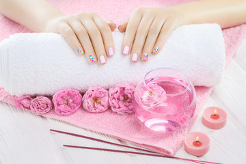 Obraz na płótnie Canvas beautiful pink manicure with tea rose, candle and towel on the white wooden table.