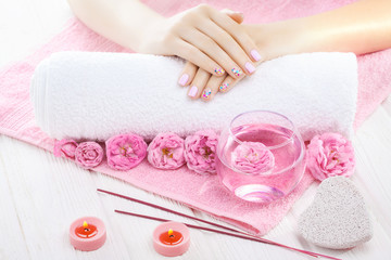 Obraz na płótnie Canvas beautiful pink manicure with tea rose, candle and towel on the white wooden table.