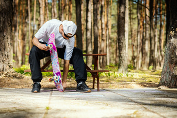 Fototapeta premium man in a white cap is sitting on a picnic table and screwing a skateboard in a summer park