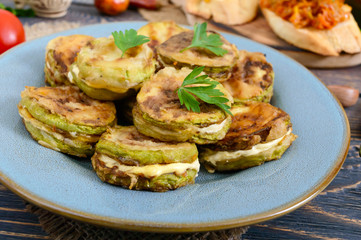 Fried pieces of zucchini with mayonnaise on a ceramic plate on a wooden table.