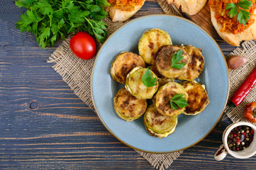 Fried pieces of zucchini with mayonnaise on a ceramic plate on a wooden table. Top view.