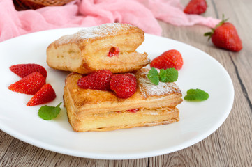 Sweet tasty puff pastry dessert on a plate on a wooden background. Delicious homemade cookies with strawberry jam, berries and sugar powder
