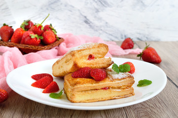 Sweet tasty puff pastry dessert on a plate on a wooden background. Delicious homemade cookies with strawberry jam, berries and sugar powder