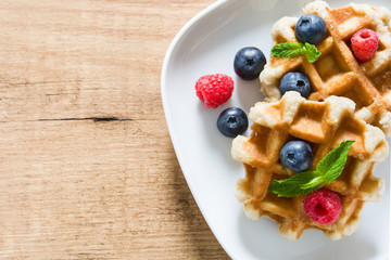Traditional belgian waffles with blueberries and raspberries on wooden table. Top view. Copyspace