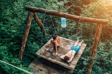 A beautiful couple resting in nature in the summer, lie and sunbathe in the sun on a wooden swing