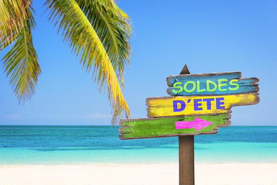 Soldes d'ete (meaning summer sale in French) written on pastel colored wooden direction signs, beach and palm tree background
