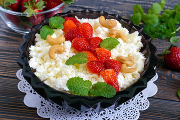 A bowl of fresh home-made cottage cheese with strawberries, mint and nuts on a wooden background. Useful breakfast. Proper nutrition.