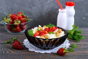 A bowl of fresh home-made cottage cheese with strawberries, mint and nuts on a wooden background. Useful breakfast. Proper nutrition.