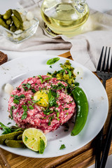 French cuisine, beef steak tartare with raw quail egg yolk, pickled cucumber and onions, fresh herbs, bread, white marble background copy space