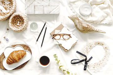 Fototapeta na wymiar Stylish flat lay of workspace in bed with cards,wooden box,croissant, glasses,cotton baskets, woman accessories on white bedsheets background.Flat lay, top view blogger influencer home office concept.