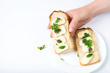 A hand holds a sandwich with cheese and greens, on a white background.