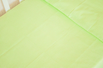 Baby bedding and quilted blanket in a white crib of tender lime green color