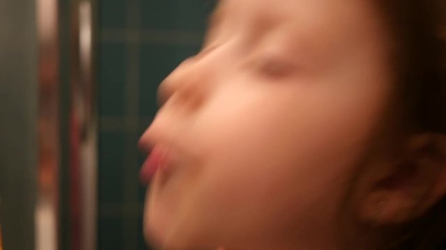 Little child girl face portrait brushing her teeth with a toothbrush in bathroom in the morning