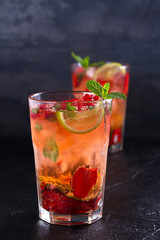 Strawberry mojito cocktail with berries, lime, mint and ice, black background. Summer berry cocktail